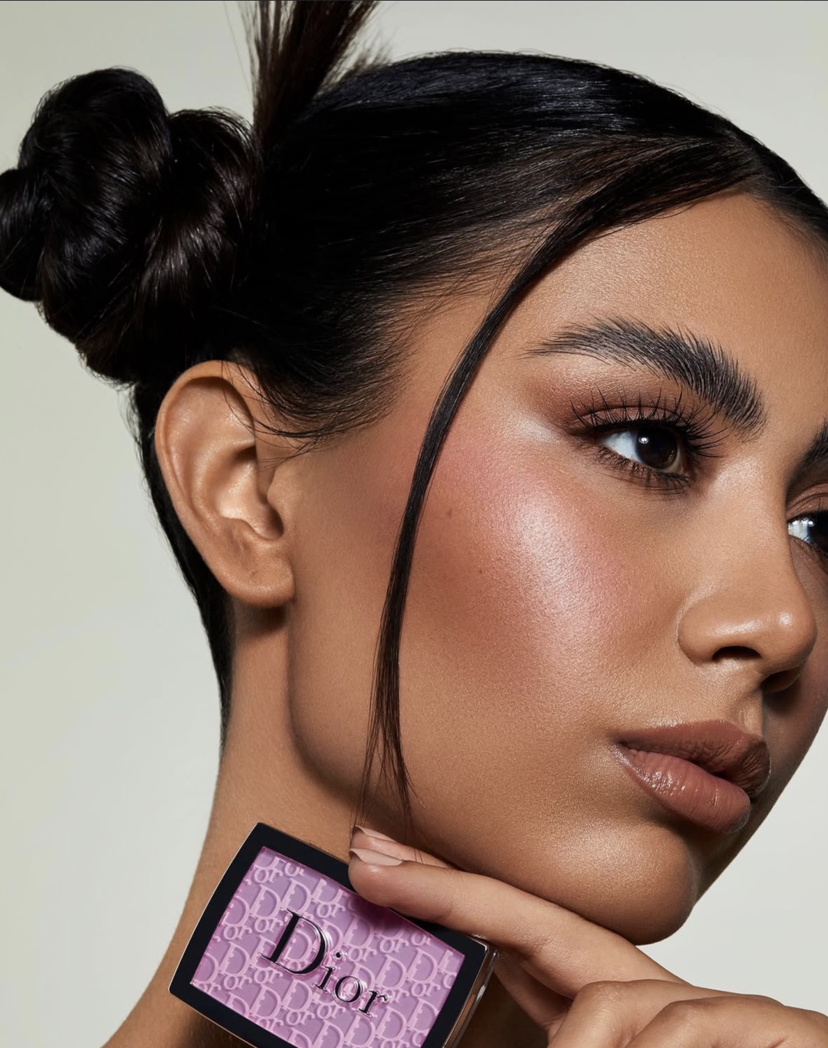Portrait of Aylin with her hair tied up, holding a Dior eyeshadow palette to her face