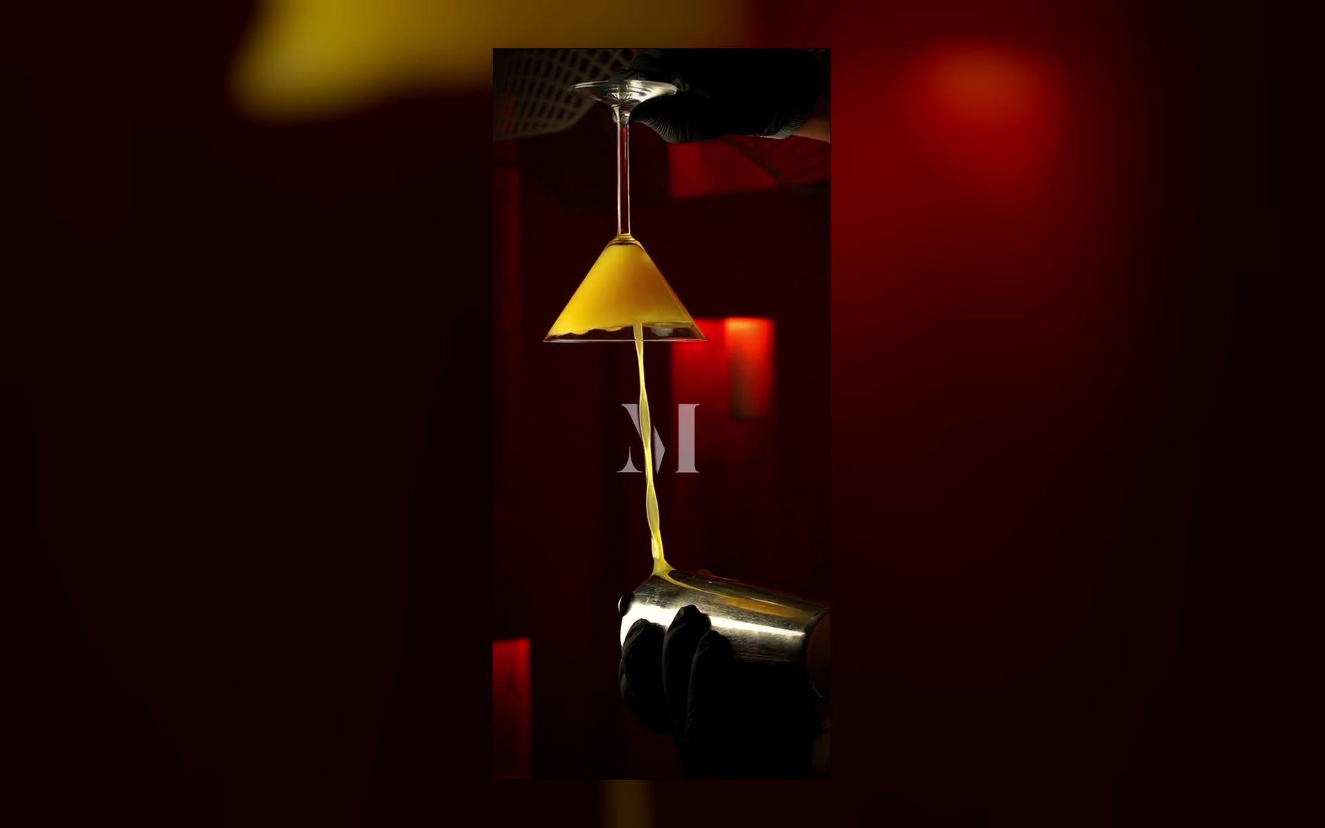 Still from the MASON’S drink clip: a yellow drink pours into an upside-down martini glass against red light